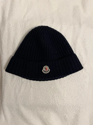 Moncler mössa  - Säljer en marinblå ribbstickad mössa från Moncler i storlek L. Men passar mig som har storlek S på andra huvudbonader. Självklart äkta som ni kan se på industri tagsen. 