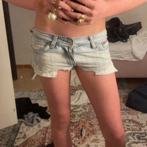 Ljusblåaa jeans shorts💓 - Säljer ett par ljusblå denimshorts från Ripelay med låg midja och råa, fransiga kanter. Shortsen har klassiska fickor fram och bak, slitningar på bakfickan och broderad text. Perfekta för sommaren eller om man ska pka utomlands🥹Midjemått- 38 cm💓
