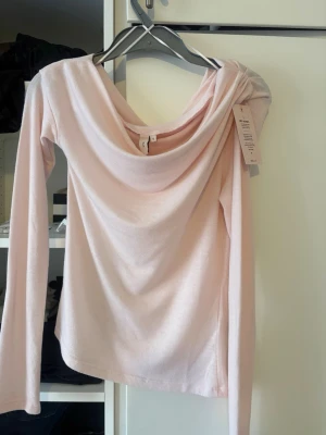 Ljusrosa offshoulder topp från Nelly - Supersnygg ljusrosa topp från Nelly med offshoulder-design och långa ärmar. Toppens material är mjukt och stretchigt, vilket gör den bekväm och smickrande. 