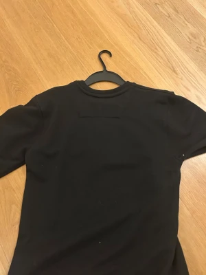 Palm Angels svart sweatshirt med björn - Svart sweatshirt från Palm Angels med broderad björn på framsidan och vit logotyptext. Tröjan har rund hals, långa ärmar och ribbade muddar. Materialet är mjukt och känns som bomull eller polyester. Perfekt för dig som gillar streetwear eller grisch stilen  och coola detaljer.