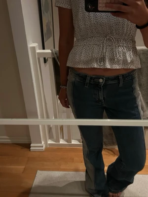 Bootcut jeans med kontrastsömmar - Säljer ett par COOLA mörkblå bootcut jeans med ljusare paneler längs sidorna och tydliga kontrastsömmar. Jeansen har låg midja och klassisk femficksdesign. Materialet är robust denim som ger en snygg vintagekänsla. Perfekt för dig som gillar en unik look.