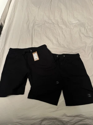 Svarta shorts från 157 med snörning stycken 2  - Svarta shorts från 157 med bekväm midja och snörning framtill. Modellen har en loose passform och är tillverkad i mjuk bomull, perfekt för chill dagar. Diskret logga nertill på benet och praktiska fickor. Snygga och enkla att matcha med t-shirt eller hoodie. Obs ett par av dom shorts är helt nya med pris lapp dom andra är använda fåtal gånger 