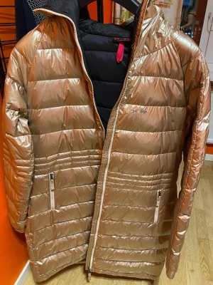 Guld pufferjacka från Skhoop XL - Säljer en riktigt snygg guld pufferjacka från Skhoop i storlek XL. Jackan har quiltad design, två dragkedjefickor och hel dragkedja framtill. Materialet är glansigt och känns lätt, perfekt för kalla dagar. Jackan har lång ärm och en cool metallic look.