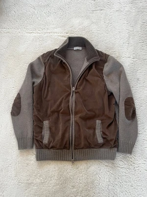 Gran Sasso brun och grå cardigan jacka - Snygg cardigan jacka från Gran Sasso i grått och brunt, med stickade muddar och krage. Framsidan och armbågarna har mockadetaljer, och jackan har dragkedja hela vägen. Tillverkad i Italien, perfekt för dig som gillar klassisk stil med en twist.