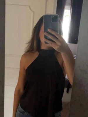 Svart halterneck linnetopp - Säljer en svart halterneck linnetopp med knyt i nacken och öppen rygg. Toppen har en lös passform och är ärmlös, perfekt för varma dagar. Materialet känns lätt och luftigt, och toppen är enkel att matcha med jeans eller kjol.