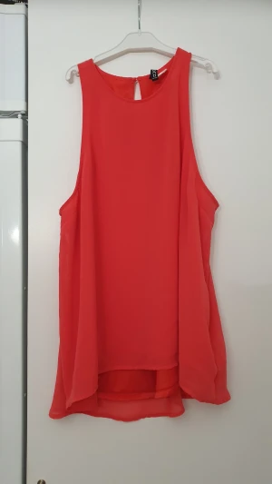 Blus - Säljer en snygg röd blus från H&M med rund hals och knapp i nacken. Blusen är ärmlös och har en flowy, lite längre passform baktill. Enkel och stilren design som ger en fräsch vibe.