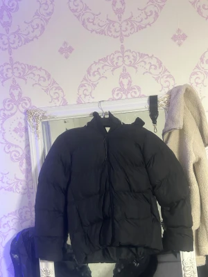 Svart pufferjacka från McKinley mer jackor finns kontakta mig för bild ock mer info  - Svart pufferjacka från McKinley med hög krage och huva. Jackan har en clean look med diskret logga på ryggen och reflexdetalj nedtill. Dragkedja framtill och två sidofickor. Perfekt för kalla dagar när du vill hålla värmen och se chill ut.