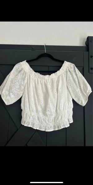 Vit broderad blus med puffärm - Supersöt vit blus med broderade blommor och puffiga korta ärmar. Offshoulder-modell med resår i halsringning och midja för en snygg passform. Perfekt för sommarens alla tillfällen!