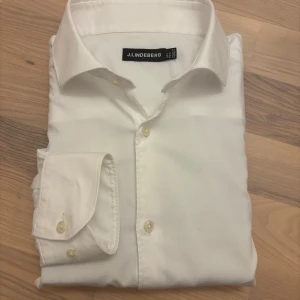 Vit skjorta från J.Lindeberg - Klassisk vit skjorta från J.Lindeberg i superslim passform. Tillverkad i 100% bomull för en fräsch och behaglig känsla. Ett stilrent och tidlöst plagg som passar både till vardag och fest.  Storlek 39 	•	Axel till axel: 42 cm 	•	Armhåla till armhåla: 46 cm 	•	Armlängd: 65 cm 	•	Längd: 77 cm