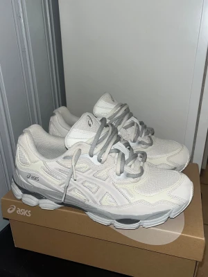 Asics GEL-NYC sneakers cream - Fräscha Asics GEL-NYC sneakers i en clean creamfärgad ton med grå detaljer. Skorna har mesh och syntetpaneler, rund tå och platt sula. Snyggt Asics-logo på sidan och GEL-dämpning i sulan för extra komfort. Perfekta för dig som gillar stilrena och sportiga sneakers.