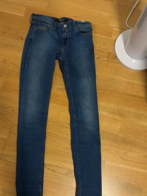 Replay Luz jeans blå 27/32 - Snygga blå Replay Luz jeans med skinny passform och klassisk femficksdesign. Jeansen har ljusa slitningar framtill och bak, samt gul kontrastsöm och läderpatch vid bakfickan. Perfekt för dig som gillar en smal siluett och stilren look.