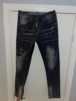 Svarta Dsquared2 jeans med tryck - Snygga svarta jeans från Dsquared2 med coolt tryck och text på vänster lår, samt färgstänk i blått och vitt. Modellen har fem fickor, skinny passform och klassisk jeanslook. Materialet är jeans och detaljerna ger en streetig vibe.