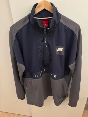 Nike Air vindjacka i marinblå och grå - Nike Air vindjacka i marinblått och grått med halv dragkedja framtill och hög krage. 