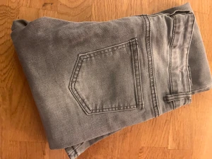 Grå bootcut jeans från D-XEL - Snygga grå jeans från D-XEL med klassisk femficksdesign och bootcut-ben. Jeansen har normal passform, bälteshällor och knappstängning framtill. Perfekt för dig som gillar en stilren look med lite retrovibe.