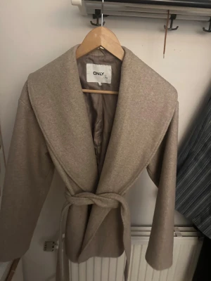 Beige kappa ONLY - Beige kappa från ONLY med knytskärp i midjan. Bra skick, perfekt nu till vintern, nypris 699kr, BUDA PÅ💖