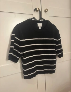Svartvit randig stickad tröja H&M - Svart stickad tröja från H&M i storlek S med vita horisontella ränder. Tröjan har rund hals, ribbade muddar och korta ärmar. Perfekt för dig som gillar klassisk stil med en modern twist.