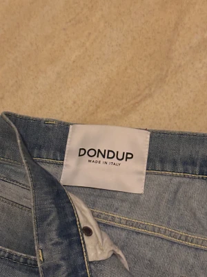 Ljusblå jeans från Dondup george - Säljer ett par ljusblå jeans från Dondup, Made in Italy. De har klassisk femficksdesign, smal passform och snygga slitningar framtill. Jeansen är tillverkade i mjukt denimtyg med diskret tvättad look och har knapp och dragkedja i midjan.