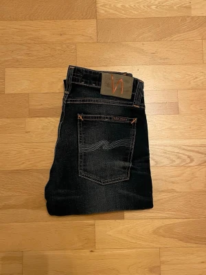 Marinblåa Nudie Jeans - Tvär feta marinblå jeans från Nudie Jeans med orangea sömmar och klassisk logga på bakfickan. Modellen är Thin Linn l passform och raka ben, med fem fickor och metallknapp framtill. Jeansen är tillverkade i slitstarkt denim och har en cool tvättad look. Tveka inte på att ställa frågor!