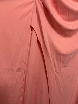 Lång offshoulder klänning i korall - Snygg långklänning i en fräsch korallrosa nyans. Klänningen är offshoulder och har draperade detaljer framtill samt en slits på sidan. Tillverkad i ett mjukt, lätt material som faller snyggt. Perfekt för dig som vill sticka ut med en elegant och trendig look.