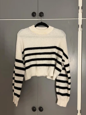 Vit och svart randig stickad tröja Nelly - Supermysig stickad tröja från Nelly i storlek M. Den är vit med svarta horisontella ränder, har en croppad passform och långa ärmar. Tröjan har en rund hals och är perfekt för dig som gillar en chill och trendig look.