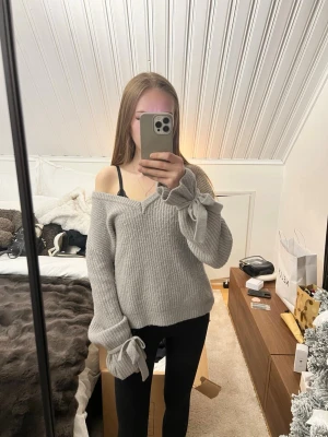 Grå stickad tröja med rosetter NA-KD - Supermysig grå stickad tröja från Linn Ahlborg x NA-KD i ribbat material. Tröjan har v-ringad hals och långa ärmar med snygga rosetter vid mudden.