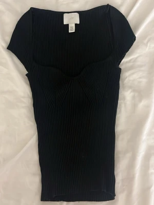 Svart ribbad topp från H&M XS - Svart ribbad topp från H&M i storlek XS. Toppen har korta ärmar. Materialet är stretchigt och ger en tight passform. 