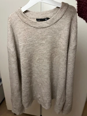 Beige stickad tröja från 157 XS - Mysig beige stickad tröja från 157 i storlek XS. Tröjan har en rundad halsringning och långa ärmar med ribbade muddar. Perfekt för lager-på-lager och chill dagar. Enkel och stilren design som funkar till jeans eller mjukis.