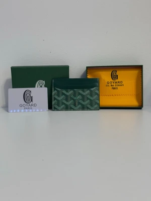 Grön Goyard plånbok med mönster - Snygg grön plånbok från Goyard med det klassiska grafiska mönstret i vitt och grönt. Slimmad design med flera fack för kort, perfekt att ha i fickan eller väskan. Kommer med original ask och certifikat. Lyxig och stilren accessoar från Paris.