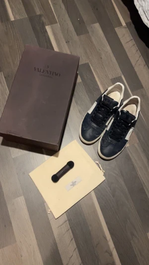 Valentino Garavani Flycrew Läder - Säljer ett par snygga Valentino Garavani sneakers i mörkblått och vitt skinn. Klassisk rund tå, svarta skosnören och vit sula. Kommer med originalkartong och dustbag. Perfekta för dig som vill ha en exklusiv och stilren look. Byter! 