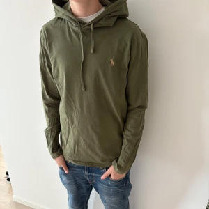 Olivgrön hoodie från Polo Ralph Lauren - Snygg olivgrön hoodie från Polo Ralph Lauren med klassisk broderad logga på bröstet. Tröjan har huva med snörning och är tillverkad i mjuk bomull. Perfekt för en avslappnad och stilren look. Långärmad modell med normal passform.