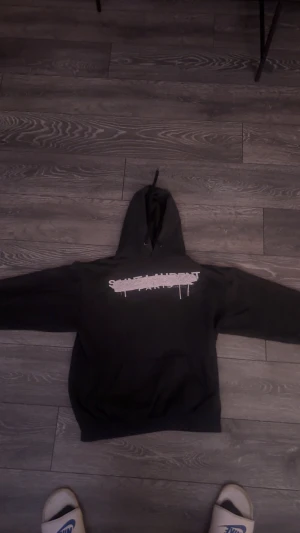 Svart Saint Laurent hoodie  - Svart hoodie från Saint Laurent med stort vitt tryck på bröstet där det står 'Saint Laurent Paris' med en cool, spraymålad effekt. Tröjan har huva med snörning och en klassisk känguruficka framtill. Perfekt för dig som gillar streetwear och exklusiva märken. Köpt på Plick men säljer igen för den it satt som jag hade velat på mig 