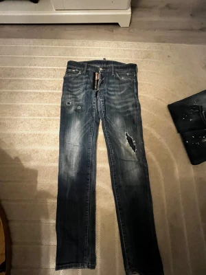 DSQUEARED2 JEANS - Ett par stilrena och enkla jeans från DSQUEARED2. Inte använda på något år och känner att de bara har plats i garderoben. Byxorna är rätt så små, passar för folk mellan 170-178cm och är relativt smala i midjan. Har behövt sy om dem lite (se bild) men förutom det har dessa jeans bara bra egenskaper.