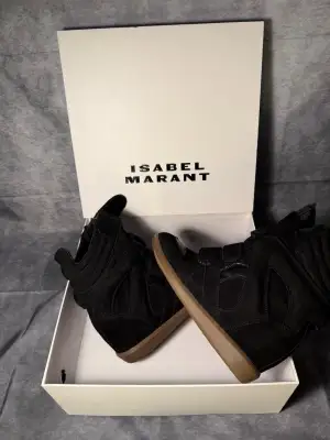 Säljer ett par svarta Isabel Marant sneakers med högt skaft och plattformssula i gummi. Skorna har en cool design med paneler i mocka och skinn, samt kardborreband för stängning. Perfekta för dig som vill ha en edgy och trendig look.
