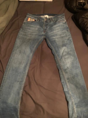 Blå jeans från Burberry London England - Snygga blå jeans från Burberry London England med klassisk Burberry-randig detalj i fickan. Jeansen är straight fit och lite slitna.