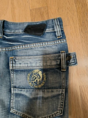Blå Diesel jeans med broderad logga - Snygga blå jeans från Diesel med slitna detaljer och broderad logga 'Only The Brave' på bakfickan. Klassisk femficksmodell med raka ben och normal passform. Jeansen har coola kontrastsömmar och etikett på framfickan. Perfekt för dig som gillar street och casual.