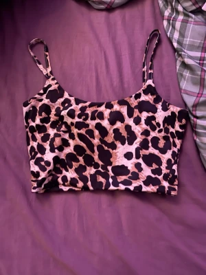 Leopardmönstrad linnetopp med smala band - Säljer en snygg leopardmönstrad linnetopp med smala axelband. Toppen har en croppad passform och är tillverkad i mjukt syntetmaterial. Perfekt för dig som vill sticka ut med ett djuriskt mönster och enkel design.