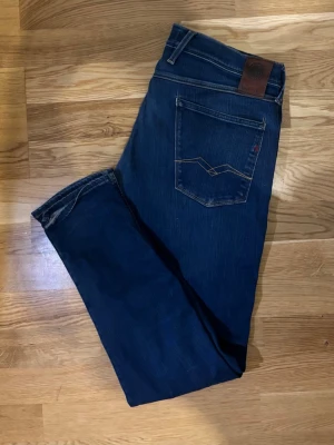 Replay Anbass - Snygga blå jeans från Replay med klassisk femficksdesign och coola kontrastsömmar på bakfickorna. Modellen är tapered med normal passform och midwaist. Materialet är slitstarkt jeans i bomull, perfekt för dig som gillar stilrena och bekväma jeans.