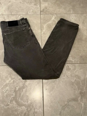 Jacob Cohën jeans - Snygga jeans från märket Jacob Cohën i en grå färg, med en svart läderpatch bak och ett broderat J på fickan gör att jeansen får en stilig look. Storleken är i W33.