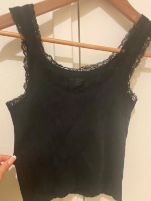 Svart ribbad topp - Säljer en svart ribbad linnetopp från Brandy Melville med breda axelband och spetsdetaljer längs kanterna 💕