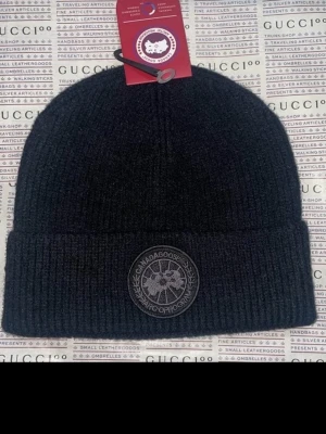 Svart ribbad mössa från Canada Goose - Snygg svart ribbstickad mössa från Canada Goose med klassisk rund logotyp framtill. Mössan har uppvikt kant och är perfekt för kalla dagar. Stilren design som passar till allt.