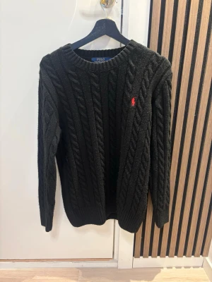 stickad tröja från Polo Ralph Lauren - Svart kabelstickad tröja från Polo Ralph Lauren med rund hals och lång ärm. Tröjan har ett rött broderat Polo-logo på bröstet och ribbade muddar vid ärmslut och nederkant. Perfekt för dig som gillar klassisk och stilren design. Kom dm för eventuella frågor 🧐pris kan diskuteras 💯