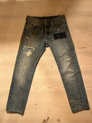 Edwin ED-80 slim tapered jeans 31/32 Japanese Salvage - Säljer ett par Edwin ED-80 slim tapered jeans i klassisk blå tvätt med slitningar och patchdetaljer. Jeansen har fem fickor, orange sömmar och selvedge-kant. Materialet är robust denim i bomull och passformen är smal med avsmalnande ben.