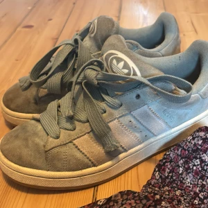 Turkosa adidas campus - Säljer ett par turkos adidas Campus sneakers i mjuk mocka med klassiska tre ränder på sidan och breda skosnören. Skorna har rund tå, platt sula och adidas logga på plösen. Perfekta för dig som gillar en clean och stilren look strl 40. Ny pris 1300kr.   
