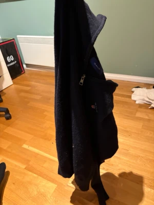 Mörkblå stickad half zip från GANT - Snygg mörkblå stickad tröja från GANT med half zip och broderad logga på bröstet. Tröjan har en klassisk krage och är perfekt för dig som gillar stilrena och tidlösa plagg. Passar dig som vill ha en enkel men ändå schysst look.