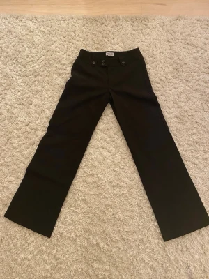 Svarta wide byxor från Madlady - Snygga svarta byxor från Madlady i storlek XS short, EU32 Short. Modellen är en vanlig midje höjd, med dekorativa knappar både fram och bak. Materialet känns som bomull och polyester, perfekt för en cool och trendig look.