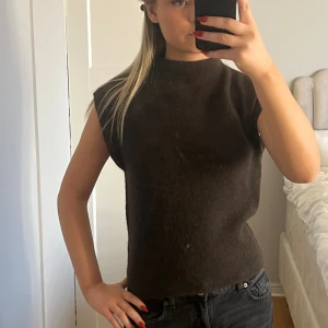 Mörkbrun ärmlös stickad tröja - Säljer en mörkbrun, ärmlös stickad tröja med lite högre hals. Aldrig använd och prislapp kvar.