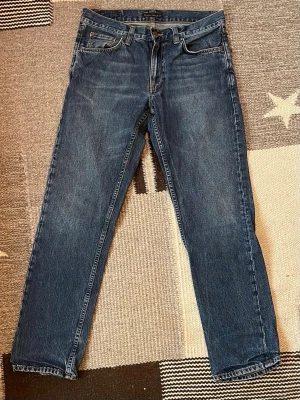 Blå jeans från Nudie Jeans - Säljer ett par klassiska blå jeans från Nudie Jeans med riktigt fin tvätt. Jeansen har modellen ”Gritty Jackson” och är tillverkade i slitstark bomull. Jeansen är använda men är i mycket bra skick. Kvitto finns!, Nypris: 1599kr. Skriv vid minsta fundering! 