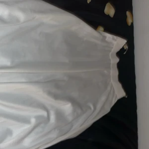 Vit långkjol i satin - Säljer en vit långkjol med glansig satinfinish och slät midja. Kjolen har en enkel och elegant design utan mönster eller detaljer, perfekt för dig som gillar stilrena plagg. Passar dig som vill ha en flowy och klassisk look.