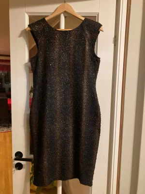 Glittrig svart kortklänning KappAhl - Snygg glittrig svart kortklänning från KappAhl i storlek 36/38. Klänningen har ärmlös design, rund hals och dragkedja i ryggen. Materialet är glittrigt och ger en festlig känsla. Perfekt för dig som vill sticka ut med lite extra glitter. Använd 2-3 gånger