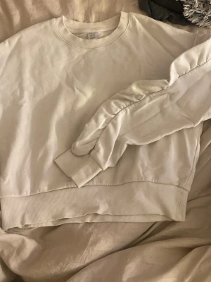 Vit tjocktröja - Volanger längst armarna. En liten blå fläck på ena armen. 